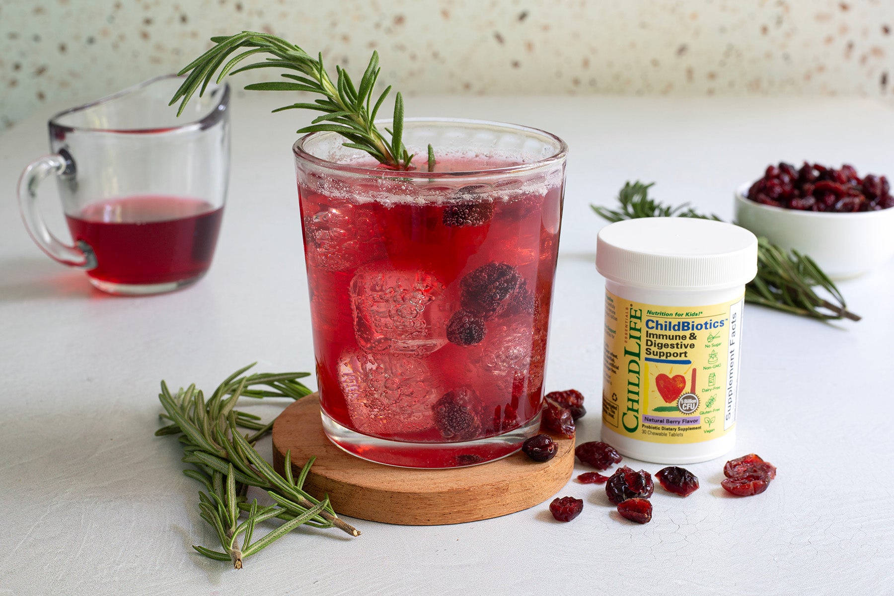 Cranberry probiotic spritzer with ice and garnish next to a container of ChildLife product on a white surface.